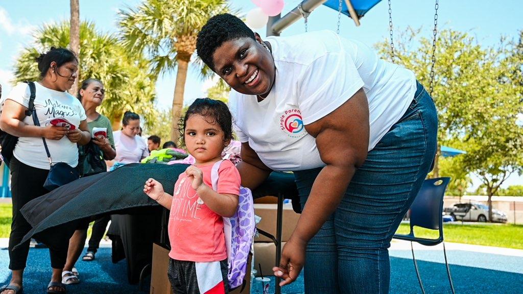 Single Parents Community Center volunteer holding hands with a young child at an outdoor family event